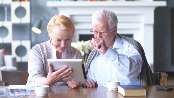 Elderly Happy Couple Working On Tablet In Modern Apartment