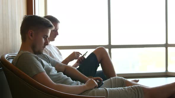 Portrait of Young Bearded Man and His Friend Sitting at Home By the Window and Chatting on Their