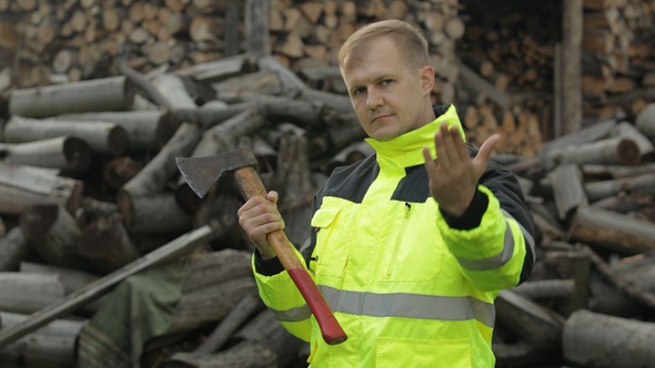 Lumberjack in Reflective Jacket, Man Woodcutter with Small Axe, Sawn Logs, Firewood Background