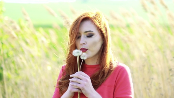 Pretty Girl With Golden Hair Blowing The Dandelion On The Background