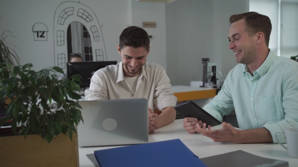 Two Workers At The Working Place Using Modern Device And Chatting About Funny News.