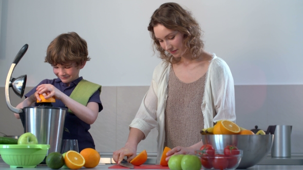 Young Caucasian Mother And Child Homemade Fresh Orange Juice In Kitchen With Electric Juicer