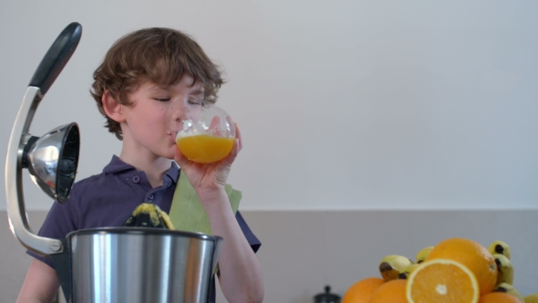 Young Funny Caucasian Boy Homemade Fresh Orange Juice In Kitchen With Electric Juicer And Drink It