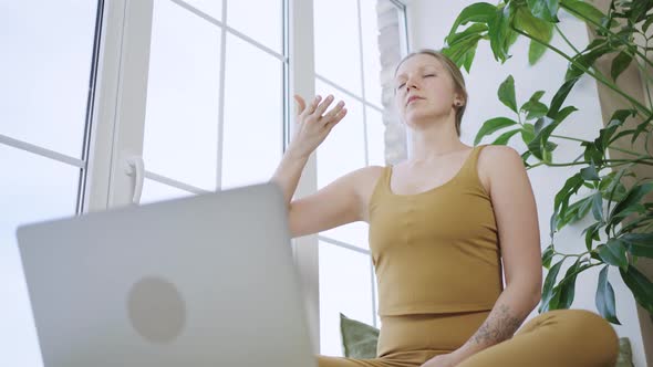 Blonde Woman in Sport Outfit Meditates Watching Tutorial