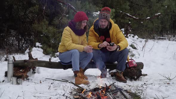 Young Woman and Man with a Phone in the Winter Forest