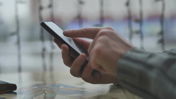 Hands of a Man with a Smartphone in a Cafe in Front of a Window and the City Writing a Message