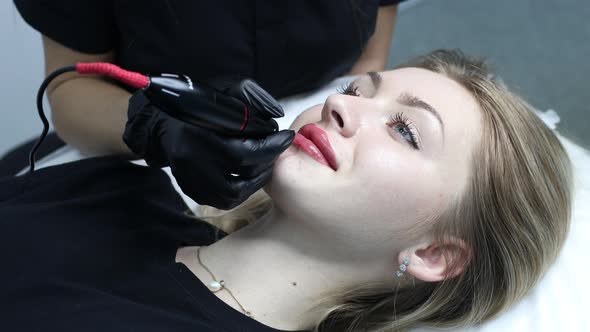 Cosmetologist Applying Pink Pigment Permanent Tattoo on Female Lips with Tatooing Needle Machine