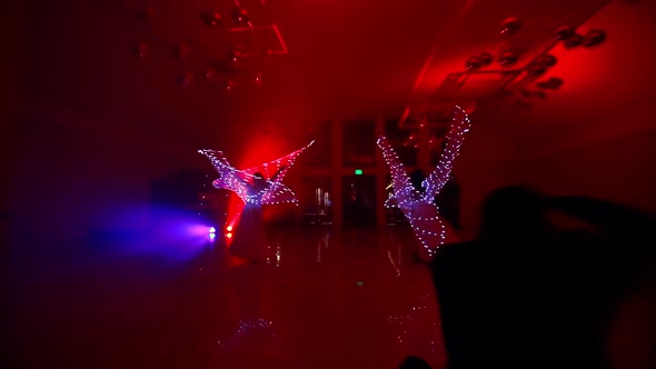 The Girls Perform a Dance with LED Wings. LED Lights and Colorful Background Glow in the Dark. Young