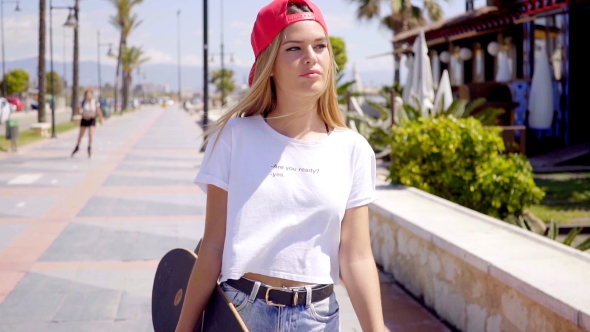 Tough Young Blond Skateboarder Walking On Sidewalk