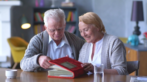 Elderly Happy Couple Looking Old Photo Album And Smiling