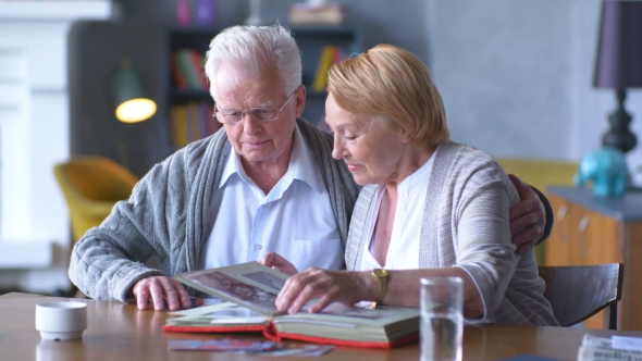 Elderly Happy Couple Looking Old Photo Album And Smiling