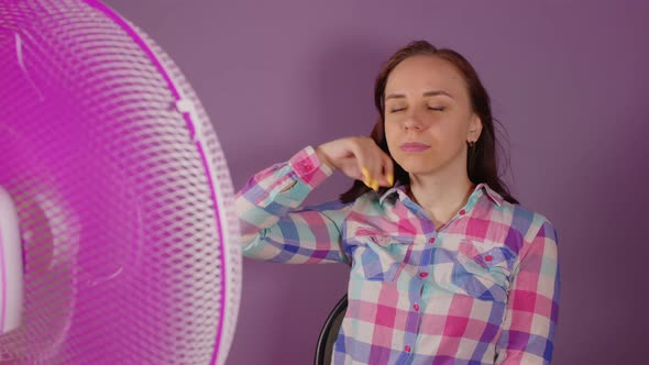 Close Up of Young Woman Sitting on Chair in Front of Fan on Purple Background