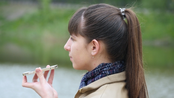 Young Woman Stands On The Embankment Of The River And Talking On a Cell Phone.