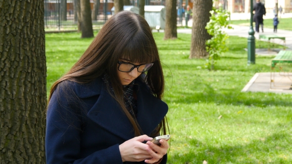 Beautiful Woman In Glasses Uses Cell Smartphone Outdoors In The Park  - Detail . Young Attractive