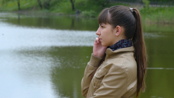 Young Woman Stands On The Embankment Of The River And Talking On a Cell Phone