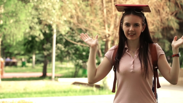 Footage Young Beautiful Woman Walking In The Park. Girl Put The Tablet On His Head.