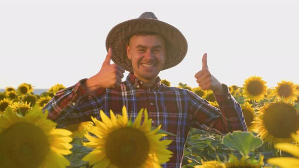 A Smiling Young Agronomist Stands in a Field Showing Thumb Up and Looking at Camera