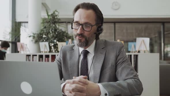 Middleaged Businessman Manager Wearing Earphones Holding Video Call Looking at Laptop Screen