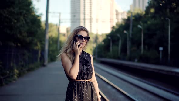 Girl Call Friend On Smartphone And Looking At Watch On Train Platform. Woman Talking On Mobile Phone