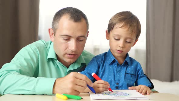 Portrait of a Happy Family. Father and Son Draw with Colored Markers, Sitting at the Table.