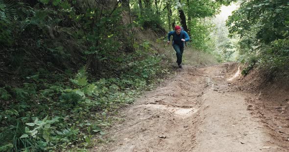 Man in a Red Bandana and a Knife in His Hand Runs Up a Steep Slope in Forest