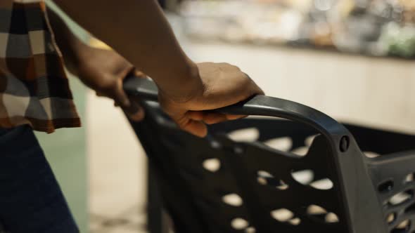 Unrecognizable Man Pushing Trolley Along Supermarket Grocery Aisle Blurred Background