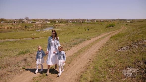 A Young Mother and Her Twin Daughters Walk Along a Country Road on a Farm