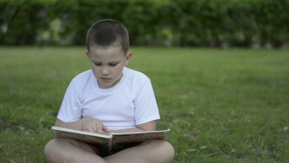 Boy Reading a Book Outdoors In a Park On The Grass. Positive Emotions