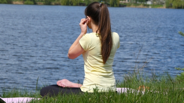 Girl putting earphones in her ears and meditating in lotus position