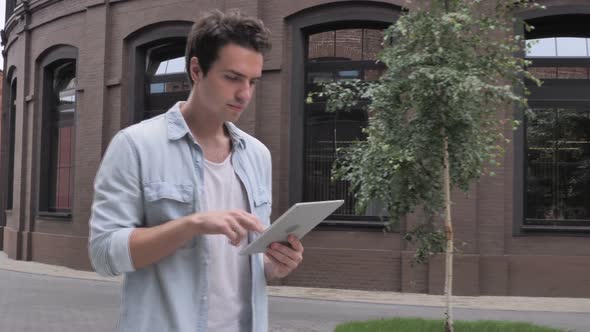 Casual Man Walking and Using Tablet Browsing Online