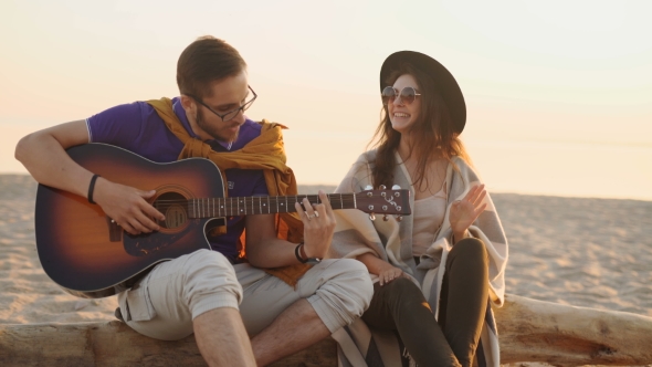 Cute Hispanic Couple Playing Guitar Serenading On Beach In Love And Embrace