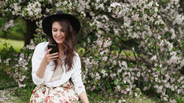 Woman Standing On The Meadow At The Blooming Tree , Using Smartphone