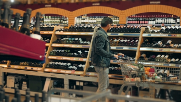 Young Man Chooses Bottle Of Wine In The Supermarket