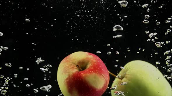 Red and Green Apples Dropping in Splash of Water Isolated on Black Background