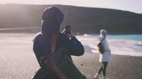 Young Loving Couple Taking Pictures on Smartphone on Beautiful Beach in Iceland During Sunset Slow