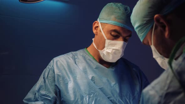 Doctor's Face in a Medical Uniform and a Mask Makes an Operation in the Operating Room