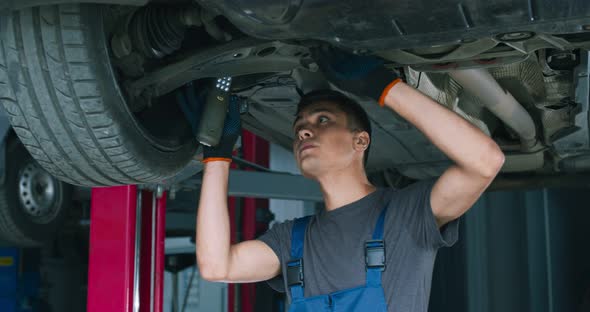 Young Male Mechanic Repairing Car Suspension, Standing Under Vehicle at Garage