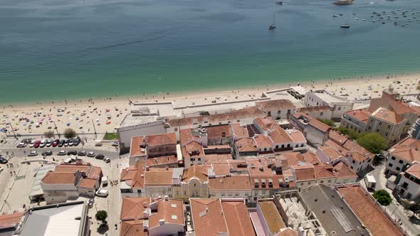 Aerial backwards of a wonderful beach and the village behind. Sesimbra, Portugal. Real time