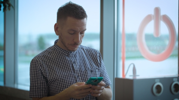 Stylish Hipster At The Airport With a Smartphone. Young Man Charges Phone At The Public Charge.