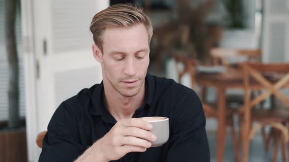 Portrait of Handsome Man Drinking Coffee in Cafe, Looks at Camera and Smiling