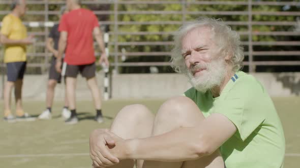 Pensive Senior Sportsman Hugging Knees with Hands Outside