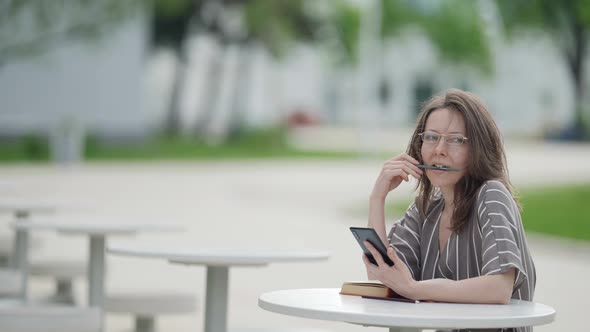 Portrait of a European Adult Female Student Reading a Book and Checking Data on the Internet While