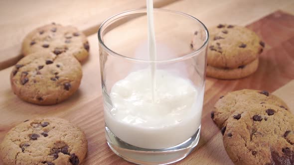 Pouring fresh milk into a glass on a table with baked oatmeal cookies with chocolate chips