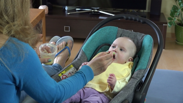 Mother Giving Food To Her Adorable Child At Home. 