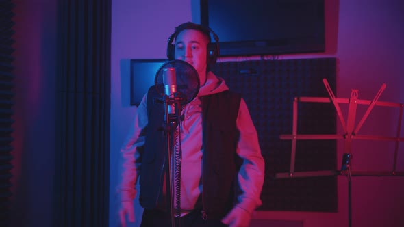 A Man in Headphones Wearing a Hoodie Rapping Through the Pop-filter in the Microphone - Recording