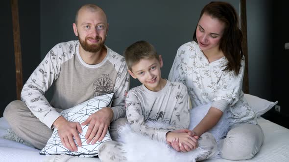 Happy Parents with Son at Bedroom, Family Photoshoot in Identicals Pajamas on Bed with Pillows