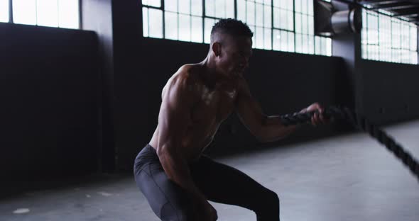 Shirtless african american man exercising battling ropes in an empty urban building