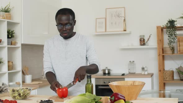 Afro Man Preparing Vegetable Salad in Kitchen