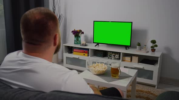 Man Watching Green Screen TV at home. Drink Beer Eating Popcorn.