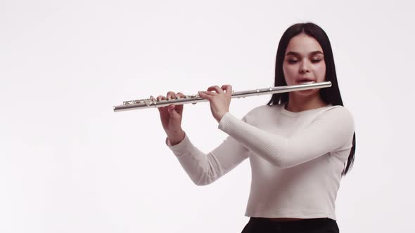 Portrait of a young Caucasian woman brings flute to her lips and starts playing on white background